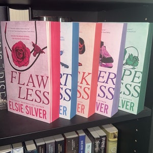 Könnte beinhalten: Ein Bücherregal mit einer Sammlung von Büchern, darunter ein Satz von vier pinkfarbenen, blauen, roten und grünen Büchern mit dem Titel "Flawless", "Artless", "Wicked", "Fierce" und "Perfect" von Elsie Silver. Die Bücher sind alle Teil einer Reihe und haben ein ähnliches Design.