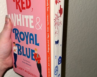 May include: A pink paperback book with the title "Red, White & Royal Blue" by Casey McQuiston. The book is a New York Times bestseller and features a quote from Taylor Jenkins Reid on the cover.