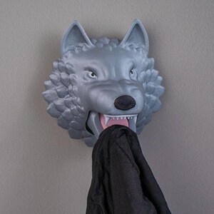 Peut inclure: Un crochet mural en forme de tête de loup gris avec un vêtement noir suspendu à sa gueule ouverte.