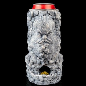 May include: A gray, stone-textured can cooler with a carved face design. The cooler has a red top and a small opening at the bottom, revealing a yellow die. The design resembles a bearded man.