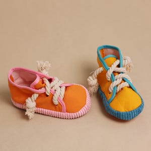 May include: Two colorful canvas shoes. One is orange with pink trim and laces, the other is yellow with blue trim and laces. Both have thick rope laces and are designed for a child.