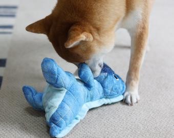 May include: A brown and white dog playing with a blue plush dinosaur toy. The dog is biting the dinosaur's head.