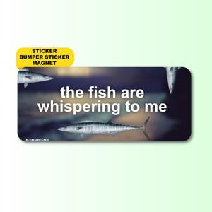Puede incluir: Una pegatina rectangular con fondo azul oscuro y marrón, tres ilustraciones de peces plateados y el texto blanco "the fish are whispering to me". Una pestaña amarilla en la parte superior izquierda dice "STICKER BUMPER STICKER MAGNET".