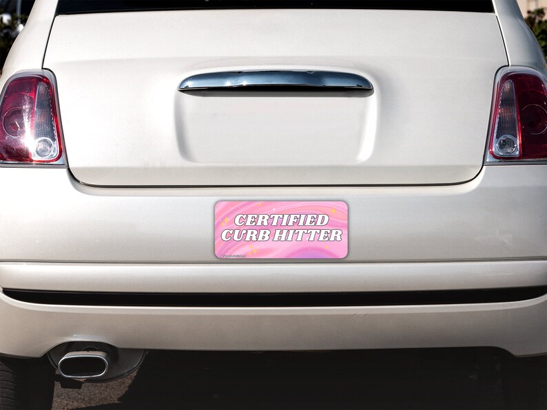 May include: A rectangular bumper sticker with a pink and purple swirled background featuring small yellow star accents. The text CERTIFIED CURB HITTER is printed in bold white capital letters with a dark outline centered on the sticker surface.