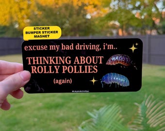 May include: A rectangular black bumper sticker featuring the peach-coloured text "excuse my bad driving, i'm.. THINKING ABOUT ROLLY POLLIES (again)". The design includes two illustrations of pill bugs and small yellow four-pointed stars.
