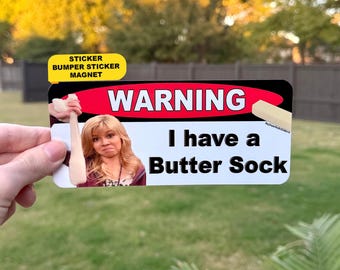 May include: A rectangular sticker featuring a red oval with the white text WARNING, an image of a person holding a sock, a stick of butter, and the black text I have a Butter Sock. The sticker has a yellow tab labeled STICKER BUMPER STICKER MAGNET.