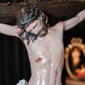 May include: A detailed sculpture of Jesus Christ on the cross. The figure has a crown of thorns, a beard, and is draped in a white cloth. The sculpture is painted with realistic skin tones and visible wounds.
