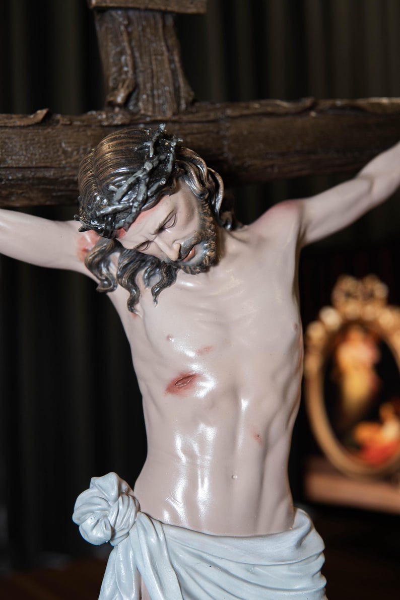 May include: A detailed sculpture of Jesus Christ on the cross. The figure has a crown of thorns, a beard, and is draped in a white cloth. The sculpture is painted with realistic skin tones and visible wounds.