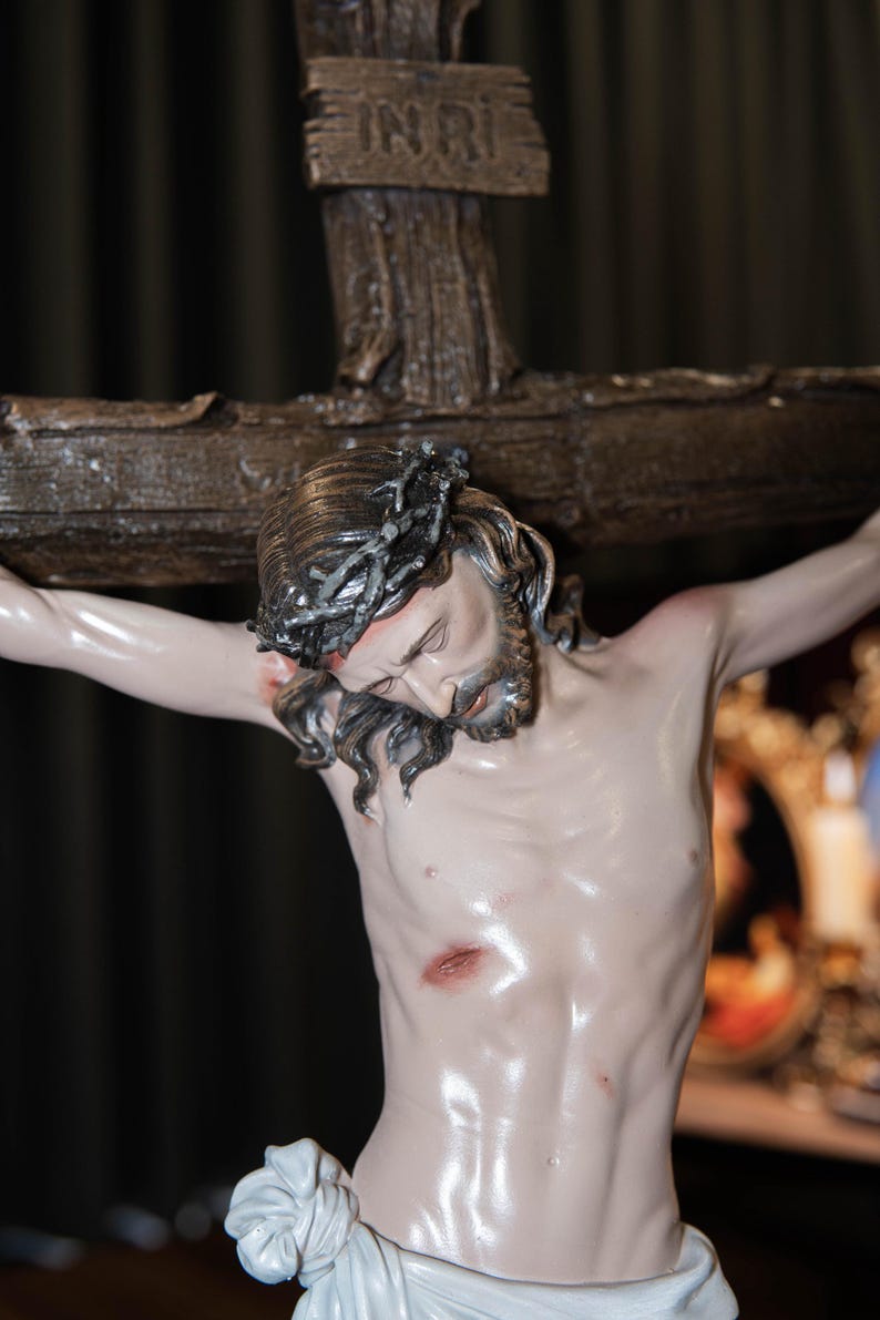 May include: A detailed statue of Jesus Christ on a wooden cross. The figure has a crown of thorns, a beard, and is draped in a white cloth. The cross has the inscription "INRI" at the top. The statue is painted with realistic skin tones.