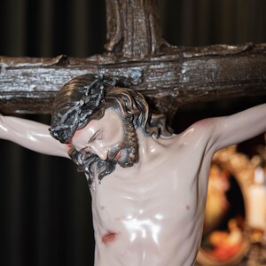 May include: A detailed statue of Jesus Christ on a wooden cross. The figure has a crown of thorns, a beard, and visible wounds. The cross has the inscription "INRI" at the top. The statue is painted with realistic skin tones and details.