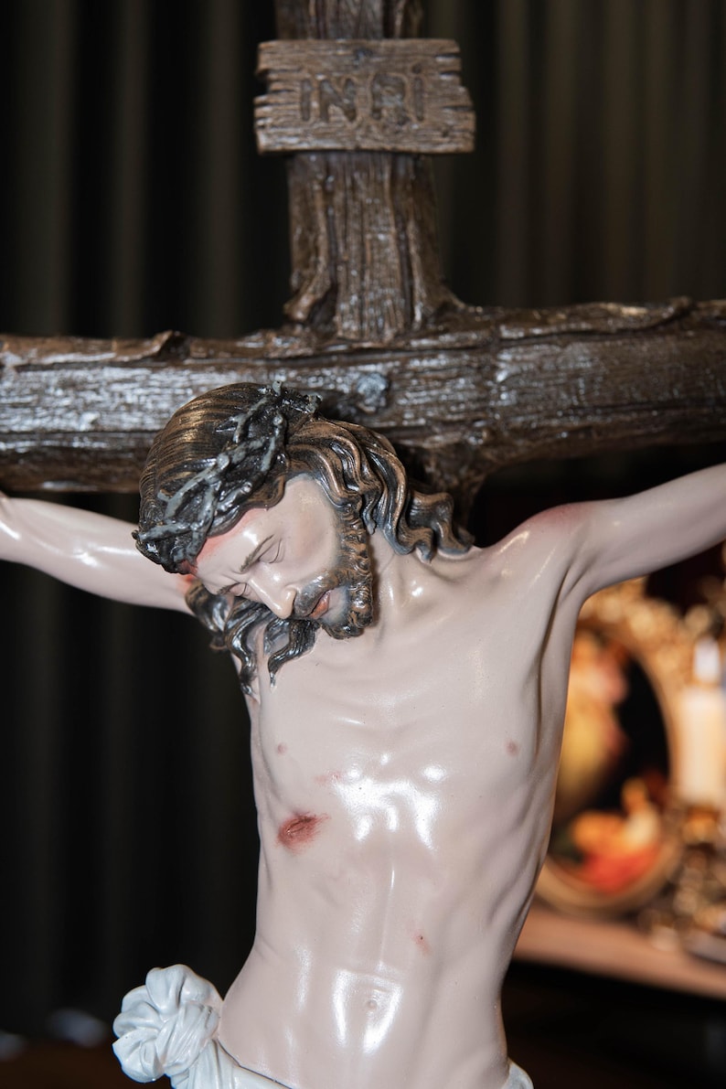 May include: A detailed statue of Jesus Christ on a wooden cross. The figure has a crown of thorns, a beard, and visible wounds. The cross has the inscription "INRI" at the top. The statue is painted with realistic skin tones and details.