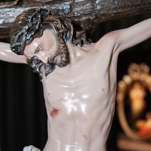 May include: A detailed sculpture of Jesus on a cross. The figure has a serene expression, with a crown of thorns and long, wavy hair. The cross is made of dark wood, and the figure is draped with a white cloth.