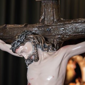 May include: A detailed sculpture of Jesus on a wooden cross. The figure has a crown of thorns, a beard, and visible wounds. The cross has the inscription "INRI" at the top. The sculpture is painted with realistic skin tones.