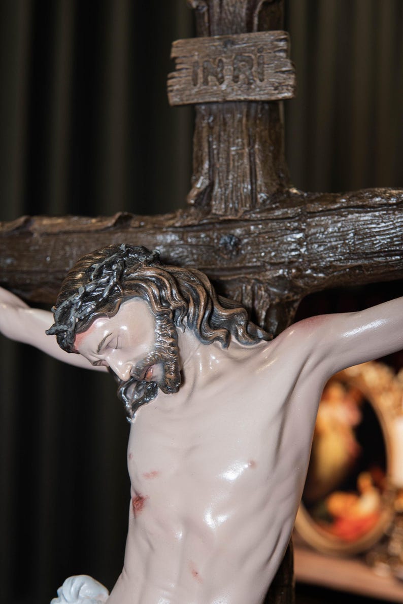 May include: A detailed sculpture of Jesus on a wooden cross. The figure has a crown of thorns, a beard, and visible wounds. The cross has the inscription "INRI" at the top. The sculpture is painted with realistic skin tones.