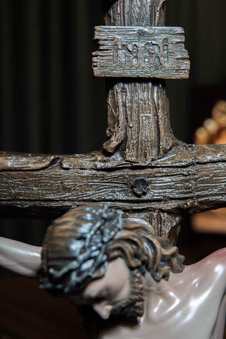 May include: A detailed close-up of a crucifix statue. The wooden cross features the inscription "INRI" on a small sign. The statue depicts a figure with a crown of thorns, with a detailed face and beard. The cross is a dark brown color.