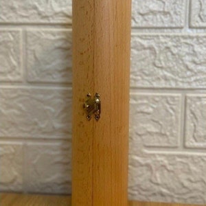Puede incluir: Una caja cil&iacute;ndrica de madera con tapa abatible y cierre de lat&oacute;n. La caja es de color marr&oacute;n claro y tiene un acabado liso.