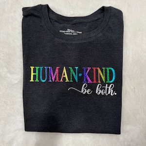 May include: A charcoal grey t-shirt with a rainbow colored "HUMAN-KIND" graphic and the text "be both." in white.
