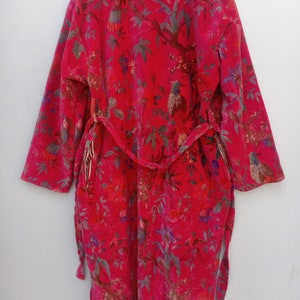 May include: A vibrant red robe with a botanical print featuring birds, flowers, and foliage. The robe has long sleeves and a matching belt. The design includes shades of green, blue, and purple, creating a colorful and detailed pattern.