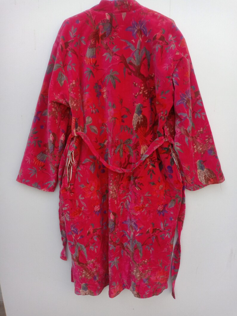 May include: A vibrant red robe with a botanical print featuring birds, flowers, and foliage. The robe has long sleeves and a matching belt. The design includes shades of green, blue, and purple, creating a colorful and detailed pattern.