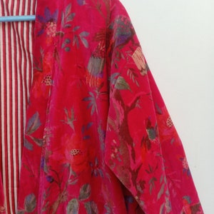 May include: A vibrant red floral print kimono-style jacket. The jacket features a bold pattern of flowers and birds in shades of pink, purple, and green. The interior lining has a striped pattern in red and white.