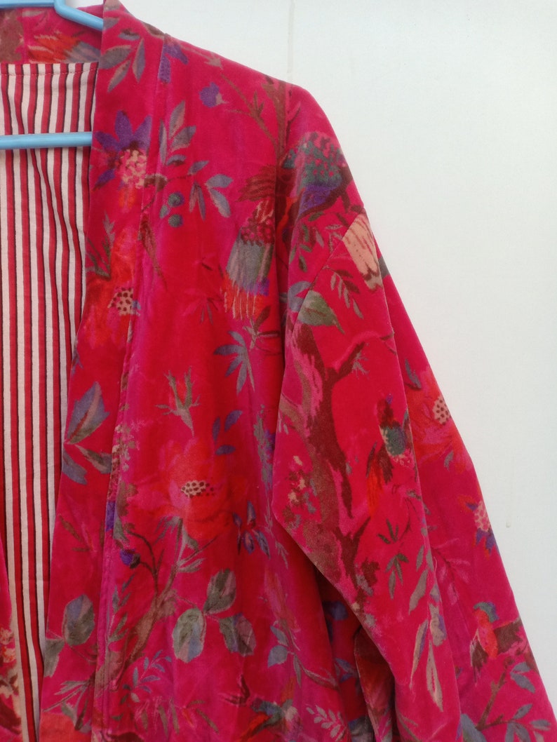 May include: A vibrant red floral print kimono-style jacket. The jacket features a bold pattern of flowers and birds in shades of pink, purple, and green. The interior lining has a striped pattern in red and white.