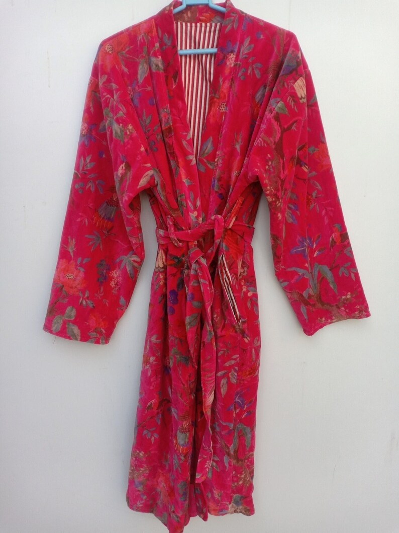 May include: A vibrant red floral patterned robe with a matching belt. The robe features long sleeves and a striped interior lining. The floral pattern includes shades of pink, green, and blue. The robe is made of a soft, velvety material.
