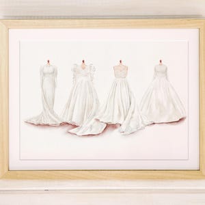 May include: Watercolor print of four white wedding dresses on mannequins. The dresses have varying styles, including long sleeves, lace details, and flowing skirts. The artwork is framed in a light wood frame.
