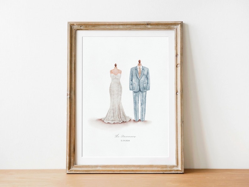 May include: Framed watercolor print featuring a wedding dress and a suit. The dress is white with a mermaid silhouette. The suit is light blue with a matching tie. The text "The [Last Name]" and a date are below the illustrations.