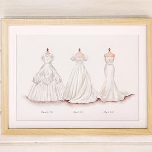 May include: A framed print featuring three white wedding dresses on mannequins. The dresses vary in style, with dates beneath each. The frame is light wood, and the background is a soft white. The print is a watercolor style.