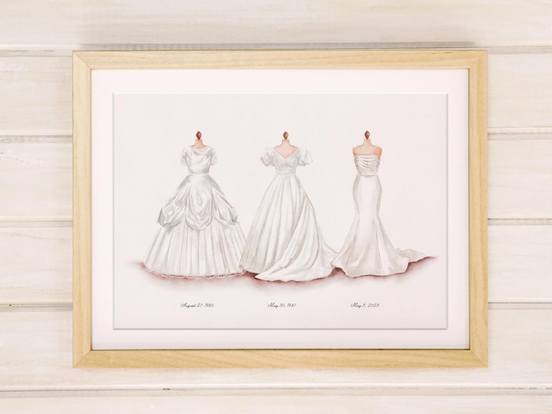 May include: A framed print featuring three white wedding dresses on mannequins. The dresses vary in style, with dates beneath each. The frame is light wood, and the background is a soft white. The print is a watercolor style.