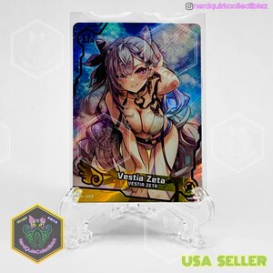 Puede incluir: Carta coleccionable con una ilustración estilo anime de Vestia Zeta. La carta tiene un acabado holográfico con tonos azules y morados. La carta se muestra en un soporte de plástico transparente.