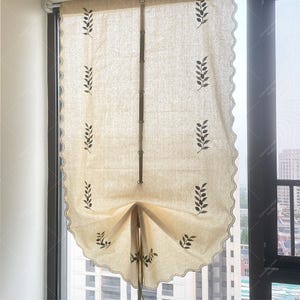 以下が含まれることがあります： クリーム色のローマンシェードで、縁が波打っていて、繊細な葉の模様が施されています。シェードは引き上げられており、街の景色が見える窓が露出しています。