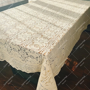 Puede incluir: Un mantel rectangular de color blanco roto que presenta un intrincado patrón de ganchillo repetitivo con motivos geométricos y florales calados. La tela tiene una apariencia texturizada y anudada con un borde festoneado.