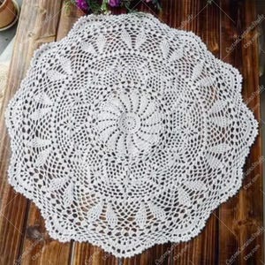May include: A white, round, crocheted doily with a detailed floral pattern. The doily features a central spiral design surrounded by intricate openwork and scalloped edges. The handmade textile is displayed on a wooden surface.
