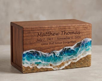 Może przedstawiać: Drewniana urna z motywem plażowym. Przód urny zawiera imię "Matthew Thomas", daty i frazę "Gone But Never Forgotten". Dół urny ma wzór piasku i fal.
