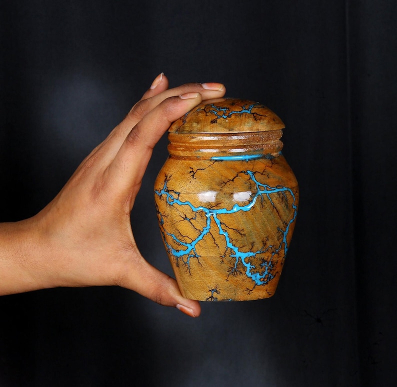 May include: A wooden jar with a lid, decorated with a blue and brown swirling pattern. The jar is hand-crafted and has a unique, artistic design.