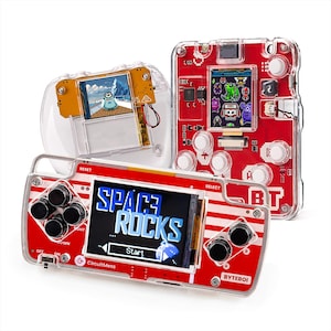 Może przedstawiać: Trzy przezroczyste i czerwone przenośne konsole do gier. Przednia konsola wyświetla na ekranie tekst "SPACE ROCKS". Pozostałe dwie konsole wyświetlają różne ekrany gier. Konsole posiadają przyciski i d-pad.