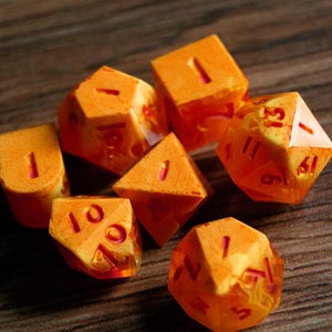 May include: A collection of orange and translucent polyhedral dice with red numbering. The dice are in various shapes, including a d4, d6, d8, d10, d12, and d20. The dice are for tabletop role-playing games.