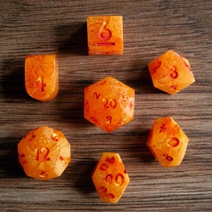 May include: Set of seven orange resin dice for tabletop games. Each die features red numbering. The dice are arranged on a wooden surface. The set includes a D4, D6, D8, D10, D12, D20, and a percentile die.