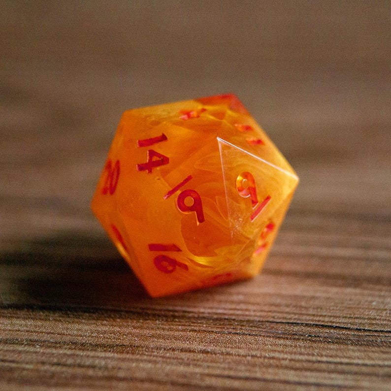 May include: A twenty-sided die with a marbled orange and yellow appearance. The numbers are in red. The die is designed for tabletop role-playing games.
