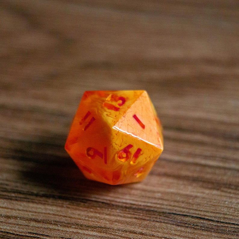 May include: A translucent orange twenty-sided die with red numbering. The die is resting on a wooden surface. The numbers are clearly visible, and the die has a slightly textured appearance.