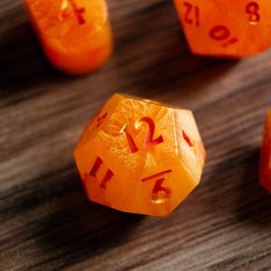May include: Close-up of several orange polyhedral dice with red numbering. The dice have a textured, marbled appearance. The dice are used for tabletop games.