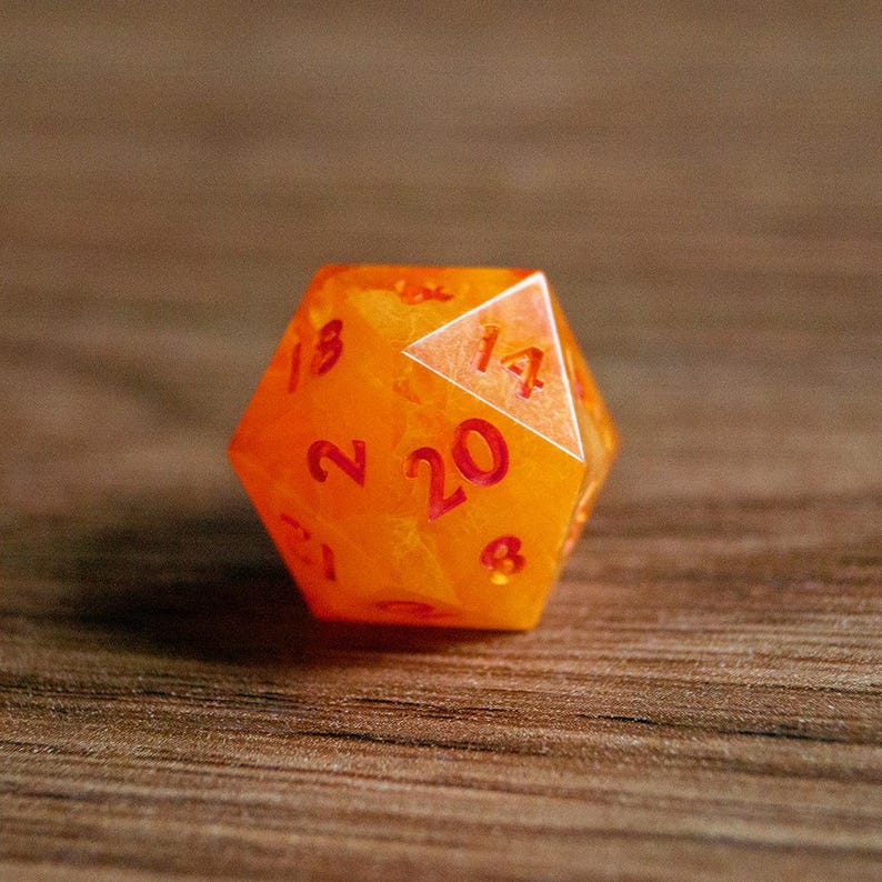 May include: An orange, twenty-sided die with red numbering. The translucent die has a marbled appearance and is set against a wooden surface. The number 20 is prominently displayed on one face.