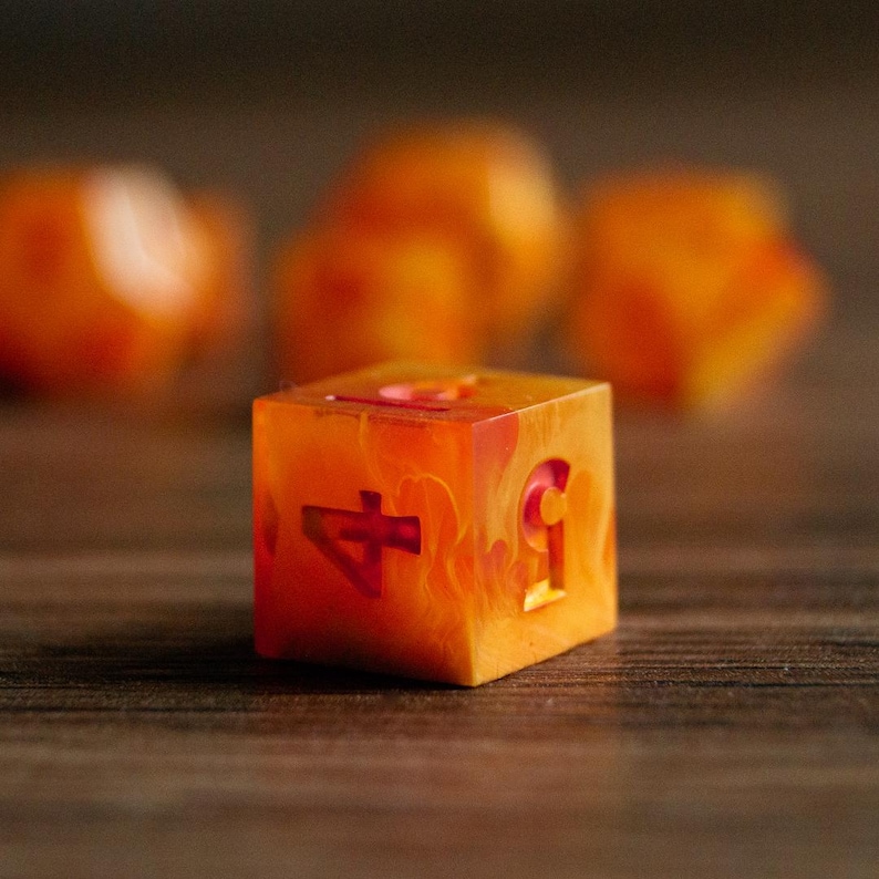 May include: A close-up of a six-sided die with the number 4 and 5 visible. The die is a translucent orange with a marbled effect. The numbers are a darker red. Other dice are blurred in the background.