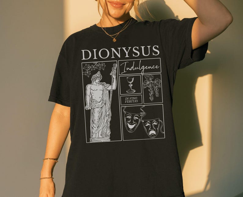 May include: Black t-shirt with a white graphic featuring the word "DIONYSUS" above the word "Indulgence". The graphic includes an illustration of a statue, a wine glass, grapes, and theater masks. The phrase "IN VINO VERITAS" is also present.