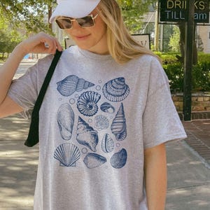 May include: A gray t-shirt with a blue and white seashell print. The shirt has a relaxed fit and a crew neck.