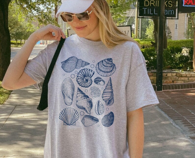 May include: A gray t-shirt with a blue and white seashell print. The shirt has a relaxed fit and a crew neck.