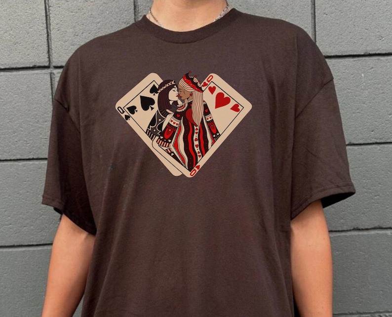 K&ouml;nnte beinhalten: Ein braunes T-Shirt mit einem Aufdruck von zwei K&ouml;niginnen aus einem Kartenspiel, die sich k&uuml;ssen. Die Herzk&ouml;nigin liegt auf der Pik-K&ouml;nigin. Der Aufdruck ist in Rot, Schwarz und Wei&szlig;.