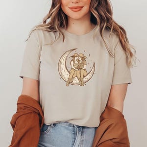 Two Sapphic Lesbian Cowgirls Sitting On Crescent Moon Tan Short Sleeve T-Shirt