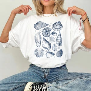 May include: A white t-shirt with a blue and white seashell print. The shirt has a relaxed fit and a crew neck.